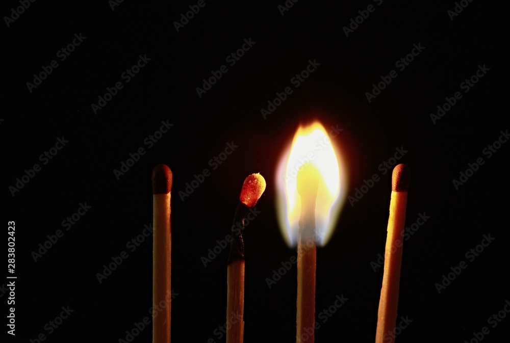 Four wooden matches on a black background. One is burnt, one is still burning and the other two are unlit. Four wooden matches on a black background. One is burnt, one is still burning and the other two are unlit.