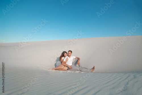 Romantic pair sit on white sand and huggins, in desert photo