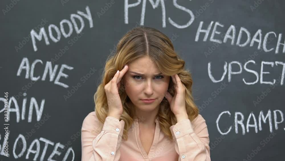 Sad woman rubbing temples suffering ache, disease symptoms written on blackboard Sad woman rubbing temples suffering ache, disease symptoms written on blackboard