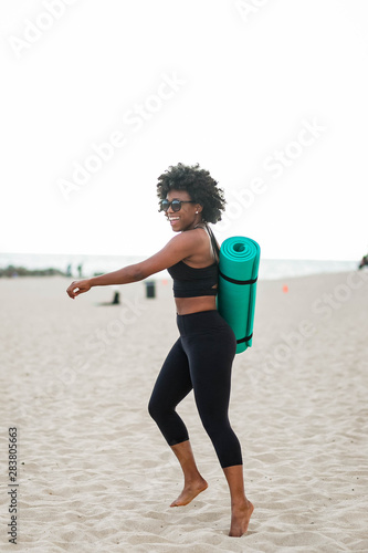 Smiling woman carrying yoga mat on beach