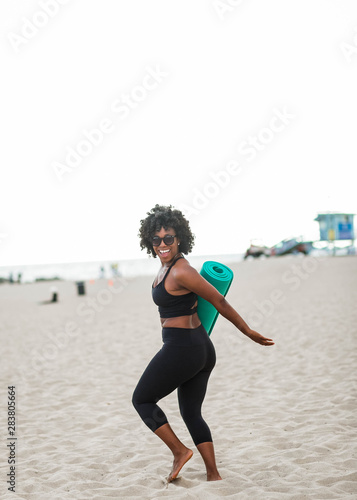 Smiling woman carrying yoga mat on beach