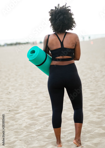 Rear view of woman carrying yoga mat on beach