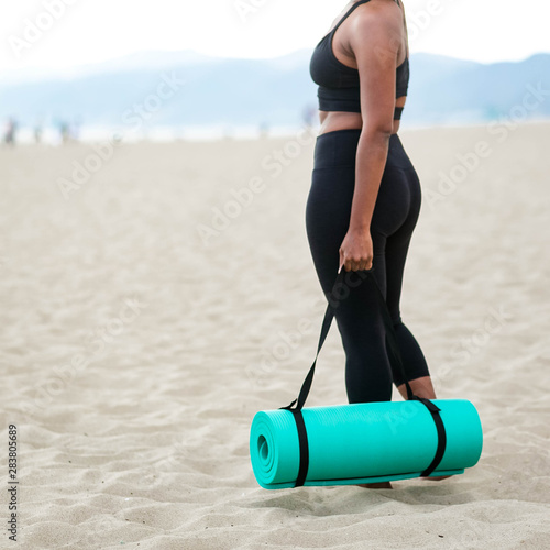 Midsection of woman carrying yoga mat on beach