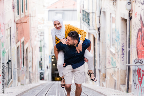 Smiling man carrying woman on back up steep street, Lisbon