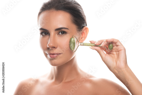 naked young woman using facial jade roller isolated on white