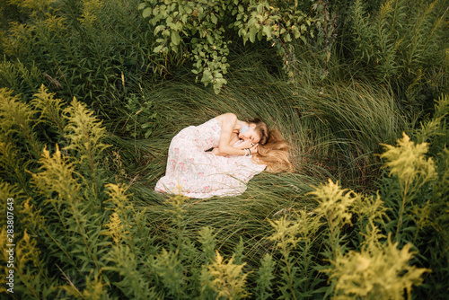 beautiful slender girl with long blonde hair in delicate dress, cute woman lies on the grass from above, fairy-tale princess in the spring garden, gentle image of the queen, fairy in love