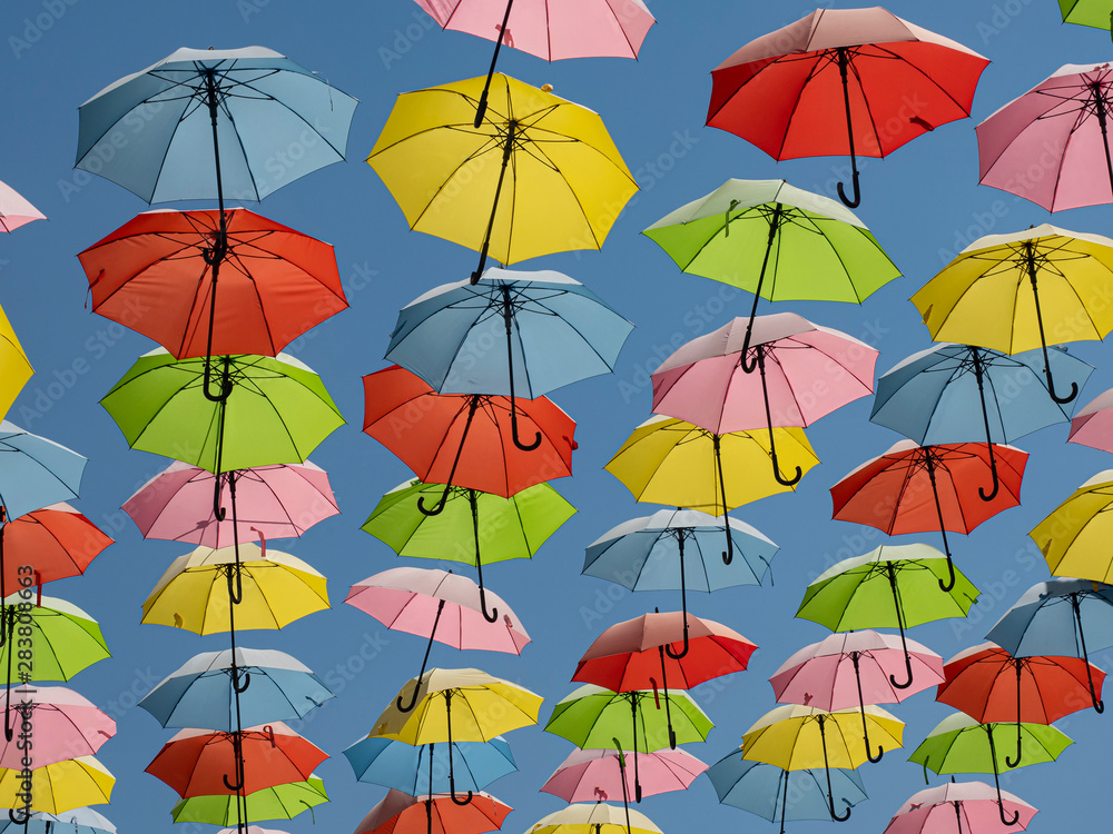Bright multi-colored umbrellas soar in the blue sky at noon in the summer heat.