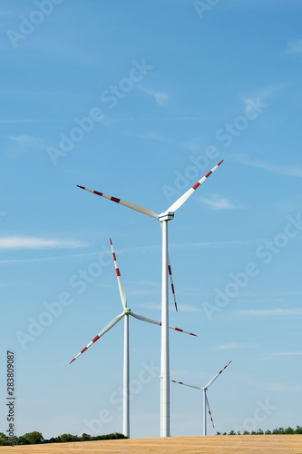 View of a wind power plant on a background of blue sky and fields with grain crops. The concept of environmental electricity production using a wind farm. © Chetgal 