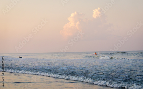 Canvas Print thunderheads loom on the distant horizon while kids engage in some surfing on th