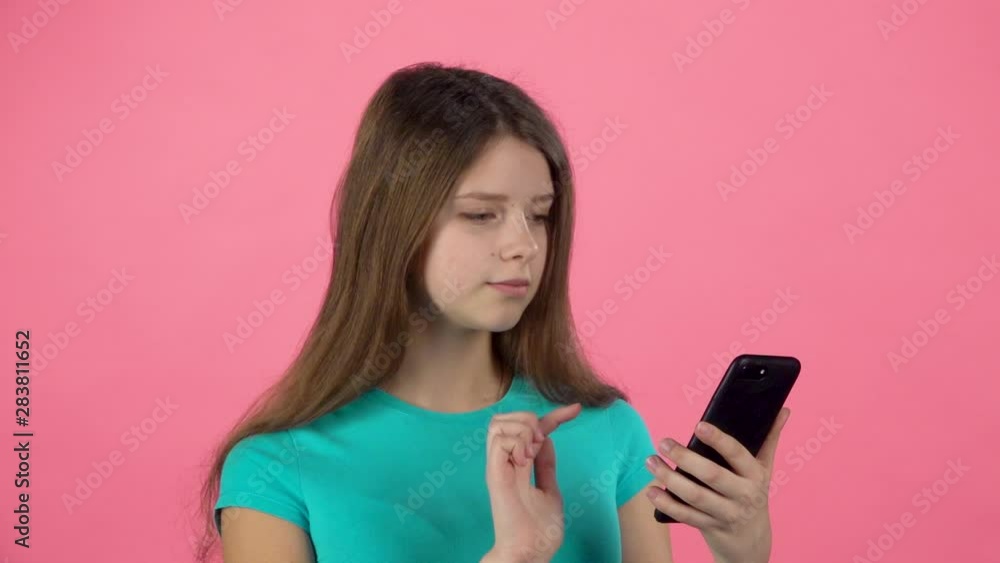 Girl talking at video chatting on cell phone in studio against pink background. Slow motion Girl talking at video chatting on cell phone in studio against pink background. Slow motion