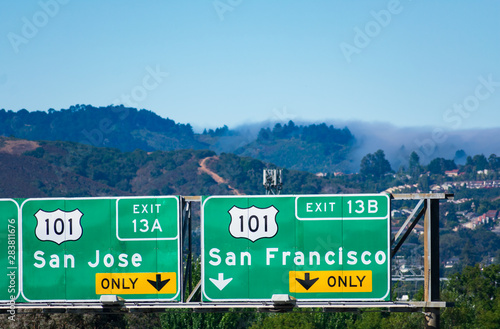 Interstate 101 highway road sign showing drivers the directions to San Jose and San Francisco in Silicon Valley. Green hills with residential area, Dense fog coming from Pacific Ocean in background photo