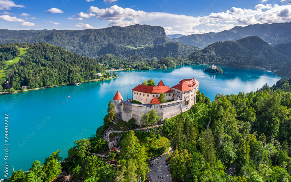 Bled, Slovenia - Aerial panoramic view of beautiful Bled Castle (Blejski Grad) with Lake Bled (Blejsko Jezero), the Church of the Assumption of Maria and Julian Alps at background on a summer day - obrazy, fototapety, plakaty 