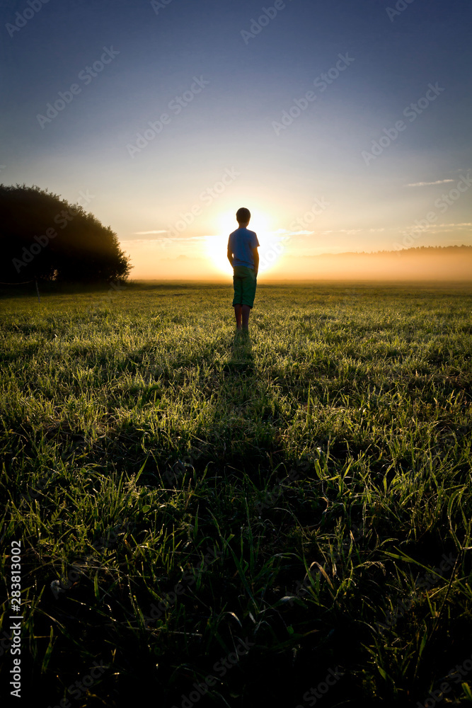 Fototapeta premium Sunrise scene. Silhouette of a boy standing in the field.