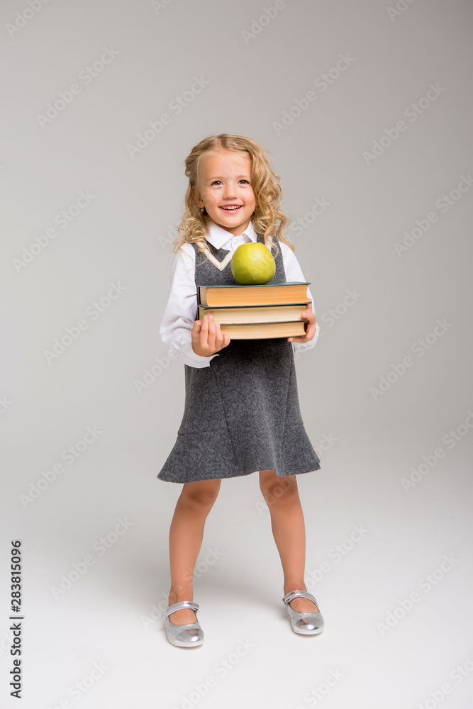 little blonde girl in school uniform with Apple and books on light background,first-grader smiling on a white background little blonde girl in school uniform with Apple and books on light background,first-grader smiling on a white background