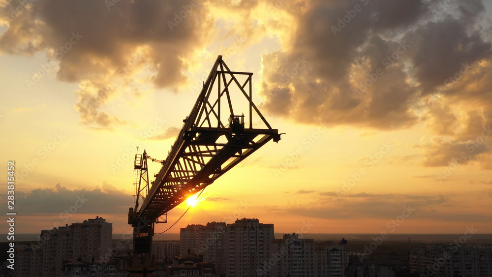 Industrial construction cranes and building silhouettes over sunset background and sunrise.
