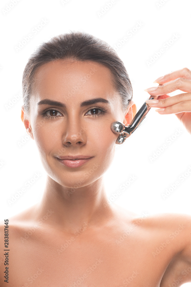 front view of naked young woman using facial massager isolated on white