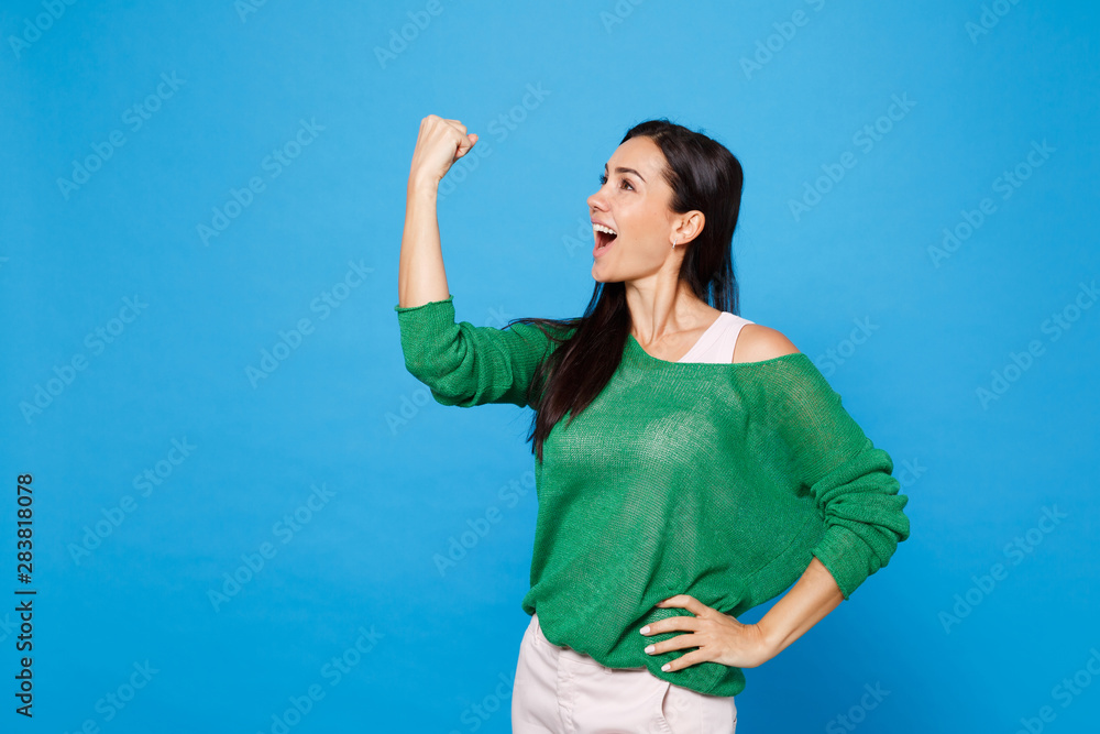 Portrait of cheerful laughing young woman in green casual clothes looking aside, doing winner gesture isolated on bright blue wall background in studio. People lifestyle concept. Mock up copy space. Portrait of cheerful laughing young woman in green casual clothes looking aside, doing winner gesture isolated on bright blue wall background in studio. People lifestyle concept. Mock up copy space.