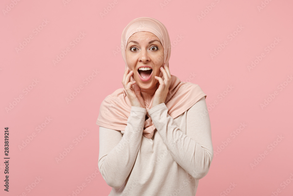 Surprised young arabian muslim girl in hijab light clothes posing isolated on pink background. People religious Islam lifestyle concept. Mock up copy space. Keeping mouth open putting hands on cheeks. Surprised young arabian muslim girl in hijab light clothes posing isolated on pink background. People religious Islam lifestyle concept. Mock up copy space. Keeping mouth open putting hands on cheeks.