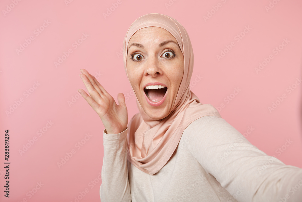 Close up amazed surprised arabian muslim woman in hijab light clothes posing isolated on pink background. People religious lifestyle concept. Mock up copy space. Doing selfie shot on mobile phone. Close up amazed surprised arabian muslim woman in hijab light clothes posing isolated on pink background. People religious lifestyle concept. Mock up copy space. Doing selfie shot on mobile phone.