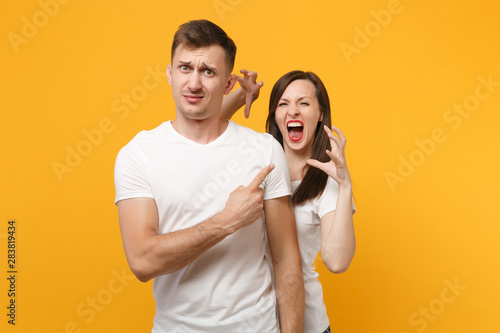 Young couple two friends in white t-shirts posing isolated on yellow orange background. People lifestyle concept. Mock up copy space. Growling like animal, making cat claws gesture, pointing finger.