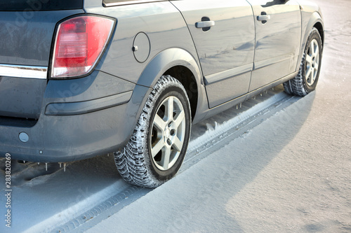 Close up of a car tire parked on snowy road on winter day. Transportation and safety concept. © bilanol