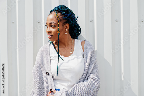 African woman with dreads hair posed against white steel wall.