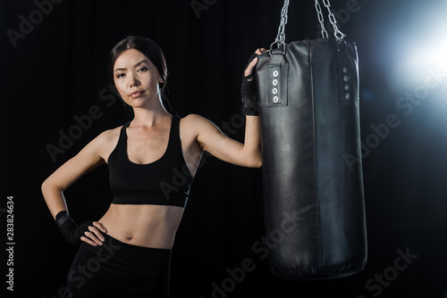 pretty girl standing with hand in hip near punching bag isolated on black © LIGHTFIELD STUDIOS