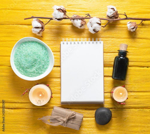 Spa blank page notepad with a copy space mockup. Bath salt, aroma oil bottle and soap on a yellow table background.