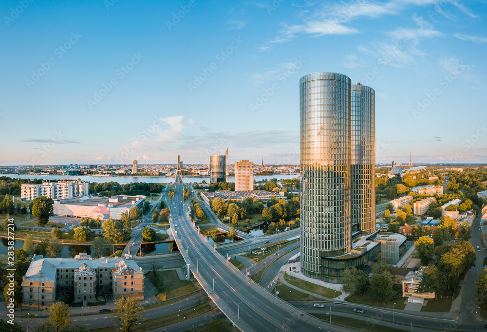 Obraz premium Panoramic, aerial view over Riga city. Modern buildings, roads, and other infrastructure. Cable bridge leading to iconic old town panorama in vivid sunset colors. 