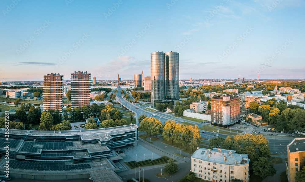Obraz premium Panoramic, aerial view over Riga city. Modern buildings, roads, and other infrastructure. Cable bridge leading to iconic old town panorama in vivid sunset colors.