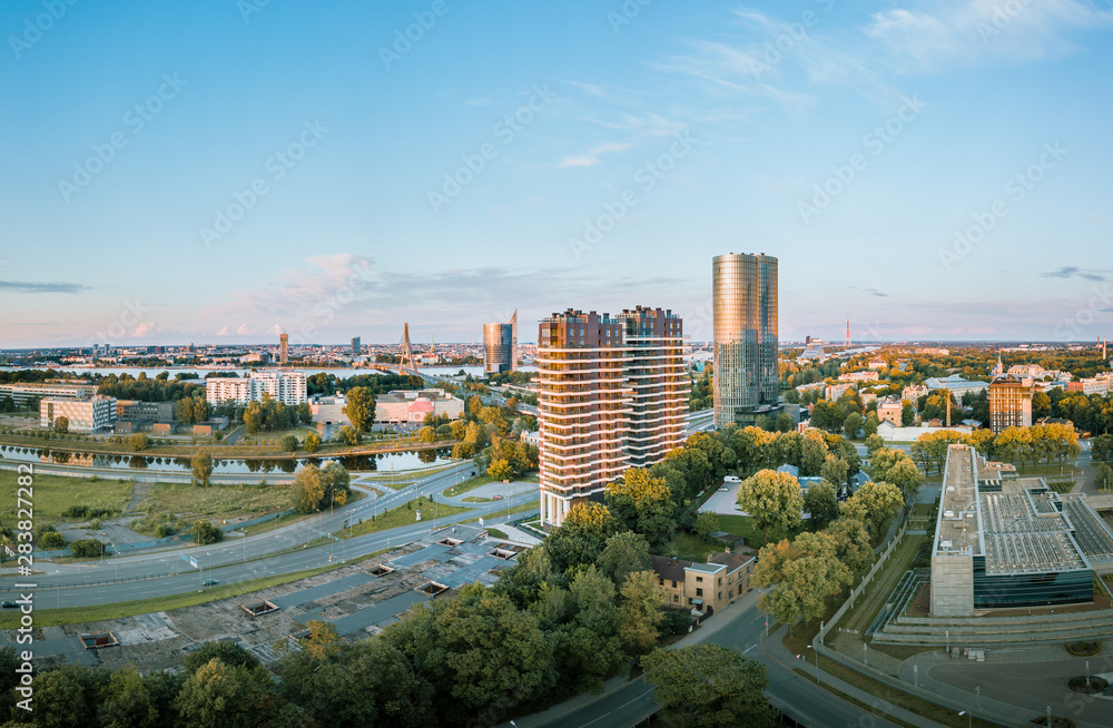 Fototapeta premium Panoramic, aerial view over Riga city. Modern buildings, roads, and other infrastructure. Cable bridge leading to iconic old town panorama in vivid sunset colors. 