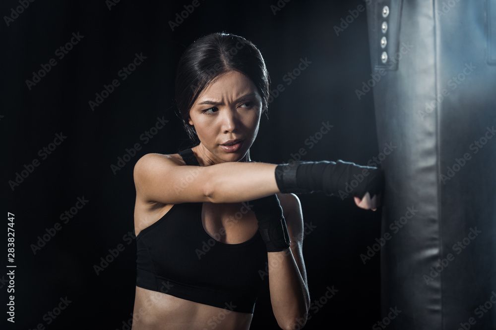 selective focus of girl working out near punching bag isolated on black selective focus of girl working out near punching bag isolated on black