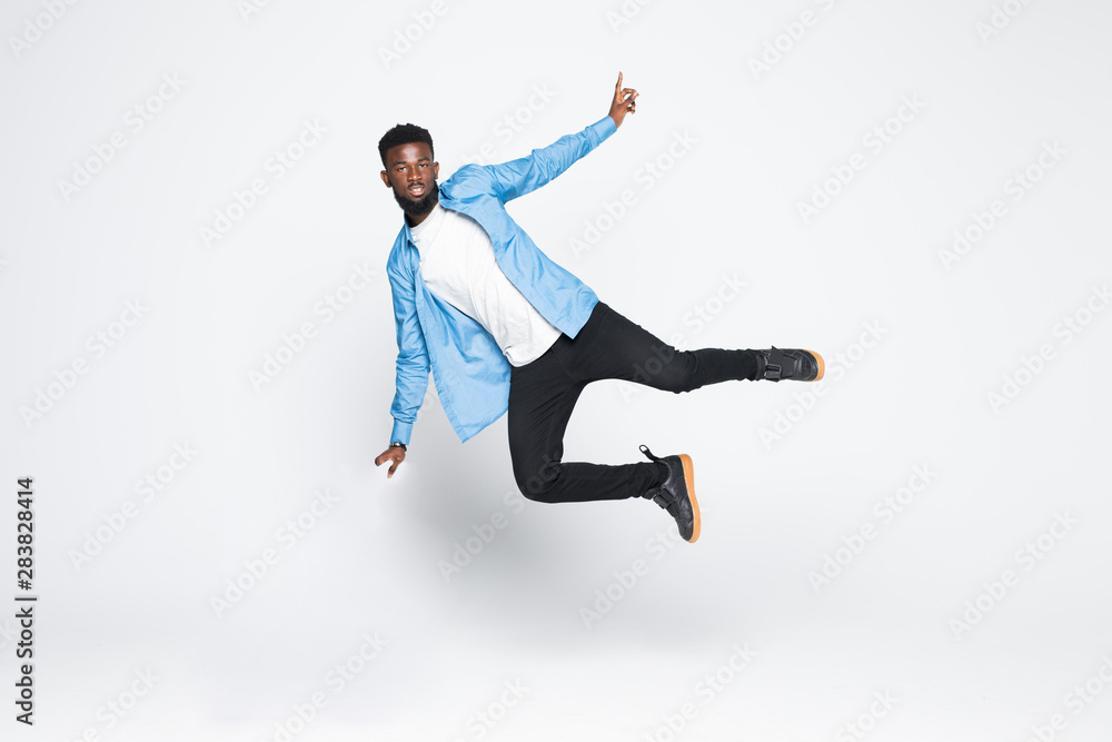 Full length portrait of cheerful handsome joyful afro man wearing casual denim jeans clothing jumping up, isolated on gray background