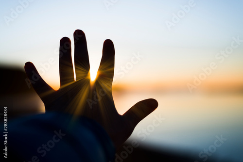 A hand is reaching for the sun with sun rays bursting thru