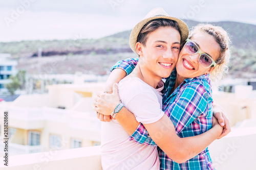 beautiful couple of mum and son together hugged in the terrace of the home having fun and laughing - woman with sunglasses and teenager with a relationship - guy with a hat hapy and funny photo