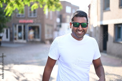 Happy and smiling black young man wearing sunglasses and walking through the city