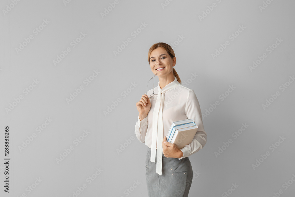 Beautiful female teacher with books on light background - obrazy, fototapety, plakaty 