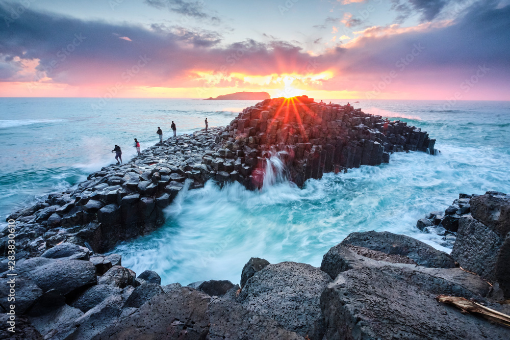 Φωτογραφία Fisherman on Giants Causeway at sunrise with red ball of the sun and nice clouds