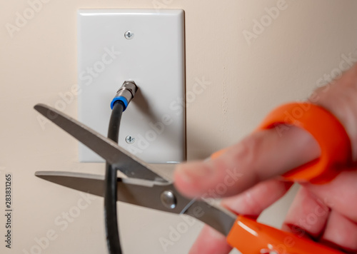 Cancelling cable TV service by cutting the coax cable connection. Close-up of male  hand using scissors to disconnect  television subscription. photo