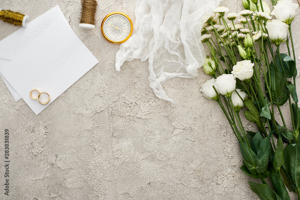 Φωτογραφία top view of wedding rings on blank invitation card, white cheesecloth and flower