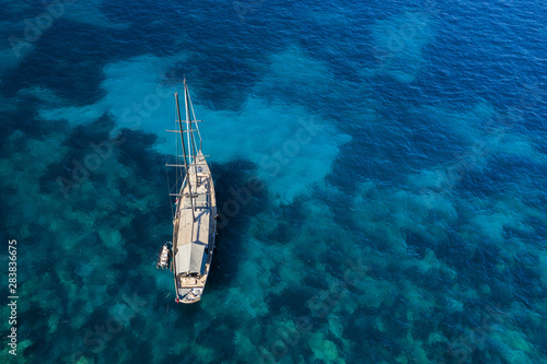 View from above, stunning aerial view of a luxury sailboat floating on a beautiful turquoise sea that bathes the green and rocky coasts of Sardinia. Emerald Coast (Costa Smeralda) Italy © Travel Wild