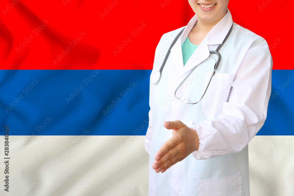 young beautiful girl doctor with an open smile holds out his hand for greeting on the background of the national flag, concepts of health care, medicine in serbia young beautiful girl doctor with an open smile holds out his hand for greeting on the background of the national flag, concepts of health care, medicine in serbia