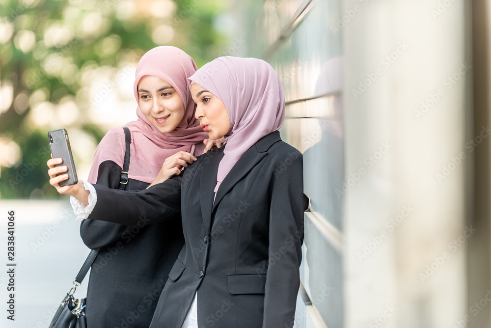 Fototapeta premium Asian Muslim girls taking a selfie. Outdoor setting.