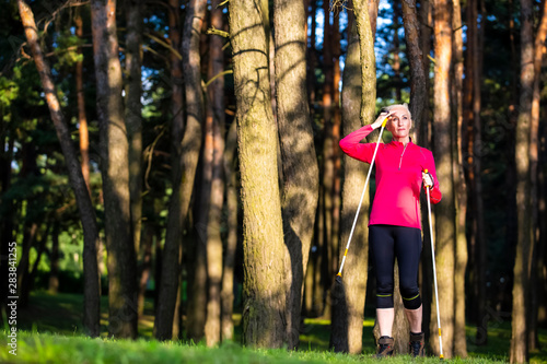 Optimistic Adult Caucasian Woman Nodic Trekking in Summer Forest Outdoors.Looking Upwards. photo