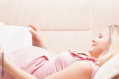 Portrait of Young Caucasian Pregnant Woman Reading on Couch Indoors.