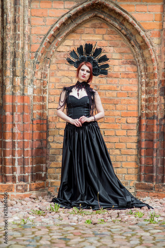 Portrait of Gothic Caucasian Woman in Black Flying Dress. Wearing Artistic Feather Crown. Posing Against Old Castle Gates. © danmorgan12