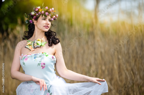 Beautiful Portrait of Caucasian Brunette Lady with Unique Flowery Chaplet and Butterflies. Posing Against Nature Background photo