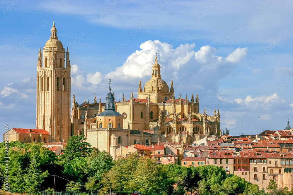 Cityscape of Segovia, Spain, depicting the gothic cathedral and the roof of some buildings with blue sky and some white clouds on blue sky composing the background