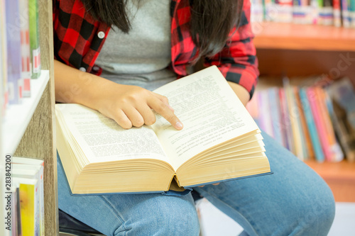 Portrait of clever student with open book reading it in college library