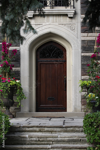 front door of gothic style stone house with floral planters and flagstone steps